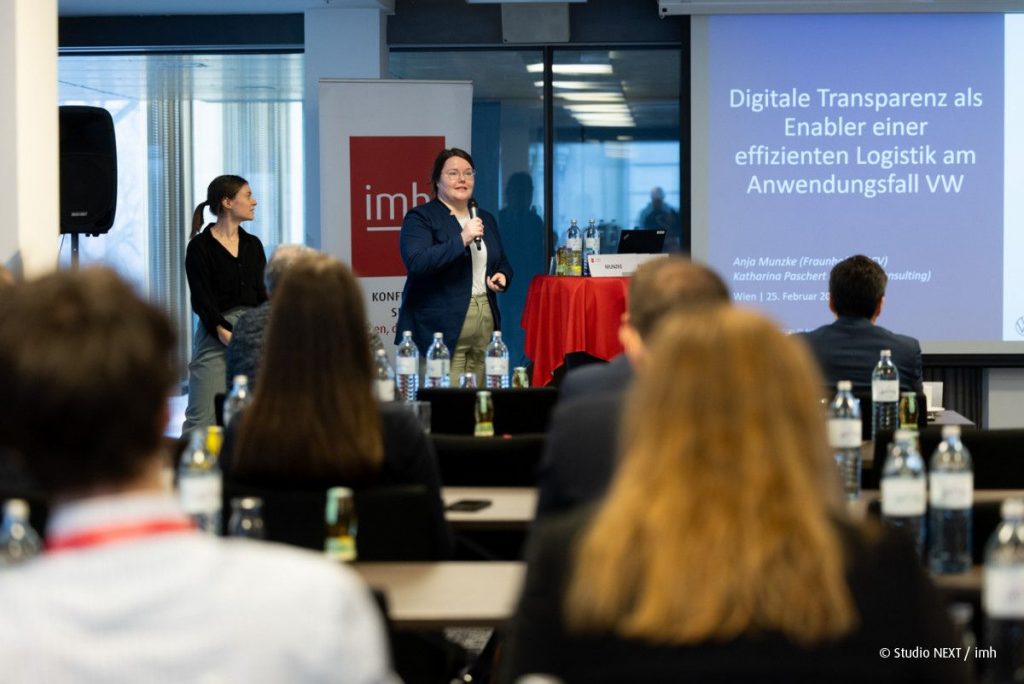 Bild, auf dem Anja Munzke (Fraunhofer IGCV) und Katharina Paschert (Ingenics Consulting) vor einem Fachpublikum einen Vortrag zum Thema Digitale Transparenz als Enabler für effiziente Logistik am Anwendungsfall VW halten. 